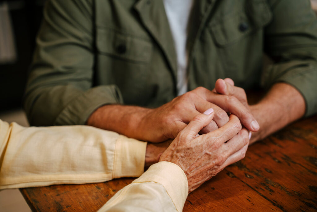 elderly couple holding hands at their kitchen table